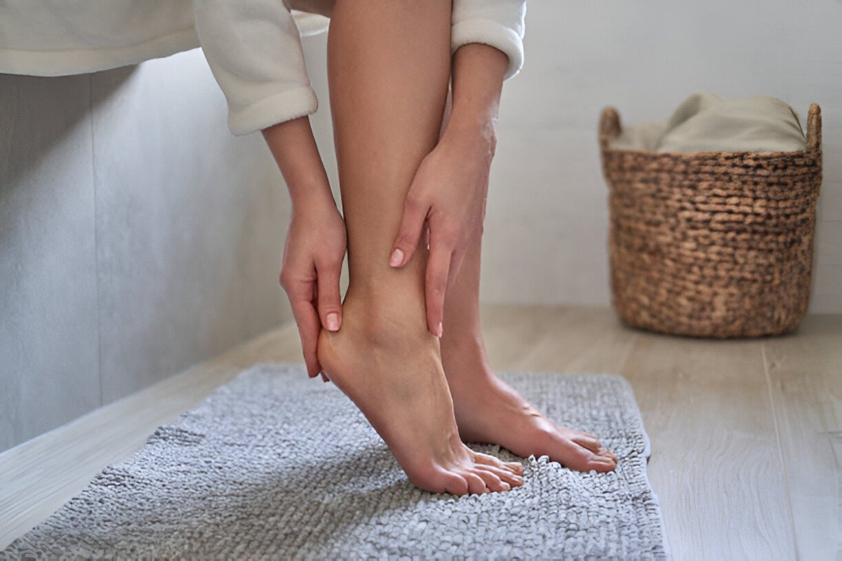 Caucasian woman in bathrobe applying moisturizing cream on heels